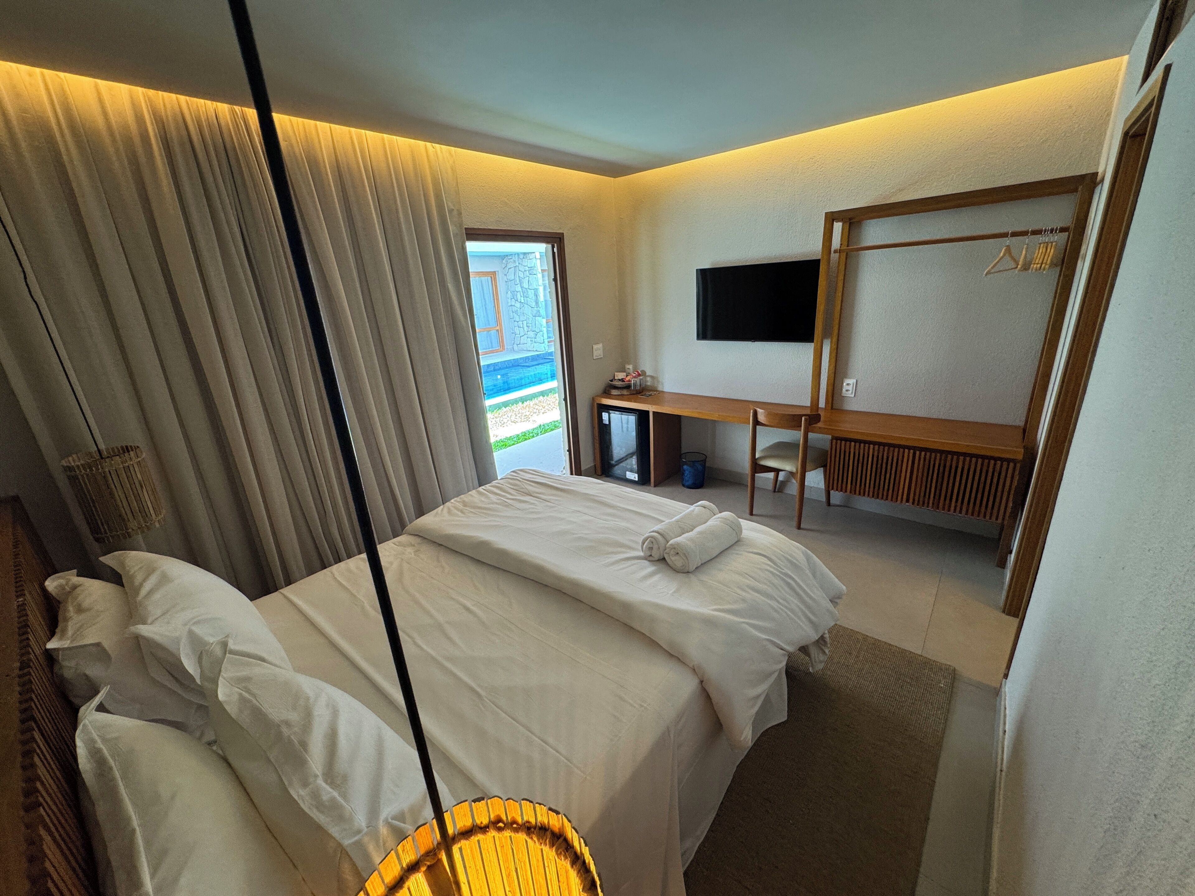Quarto de hotel com cama, escrivaninha, cadeira, televisão e vista para o exterior.