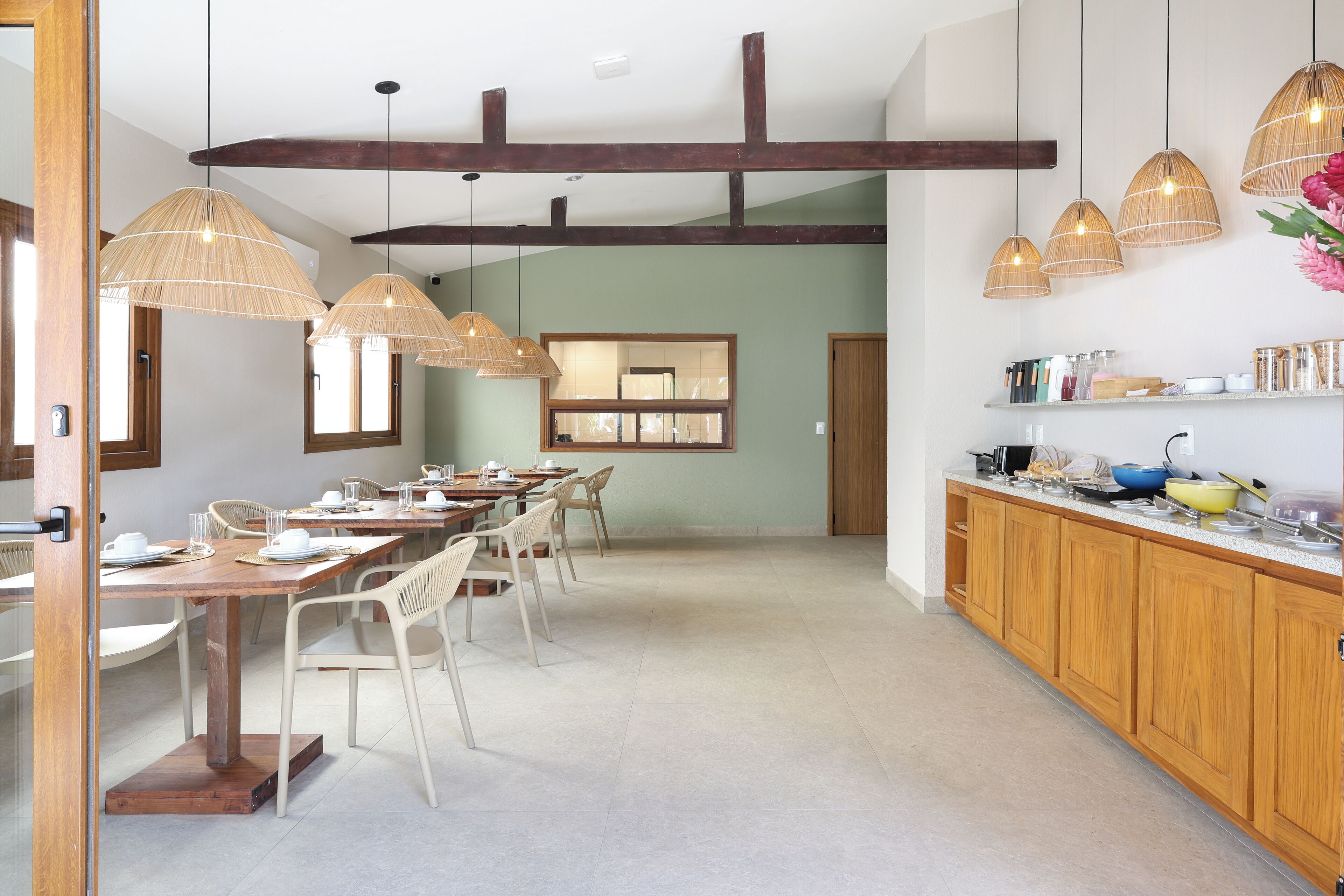 A spacious dining area with a long wooden table and chairs, a kitchen area with wooden cabinets and a countertop, and hanging bamboo lamps.