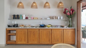 Uma cozinha com armários de madeira, bancada com diversos utensílios e três luminárias pendentes.
