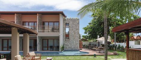 Un edificio de dos plantas con fachada de piedra, piscina, mobiliario exterior y un césped bien cuidado.