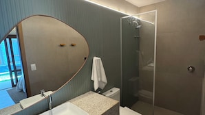 Um banheiro moderno com um espelho grande, bancada de granito, pia branca, vaso sanitário e box de vidro.