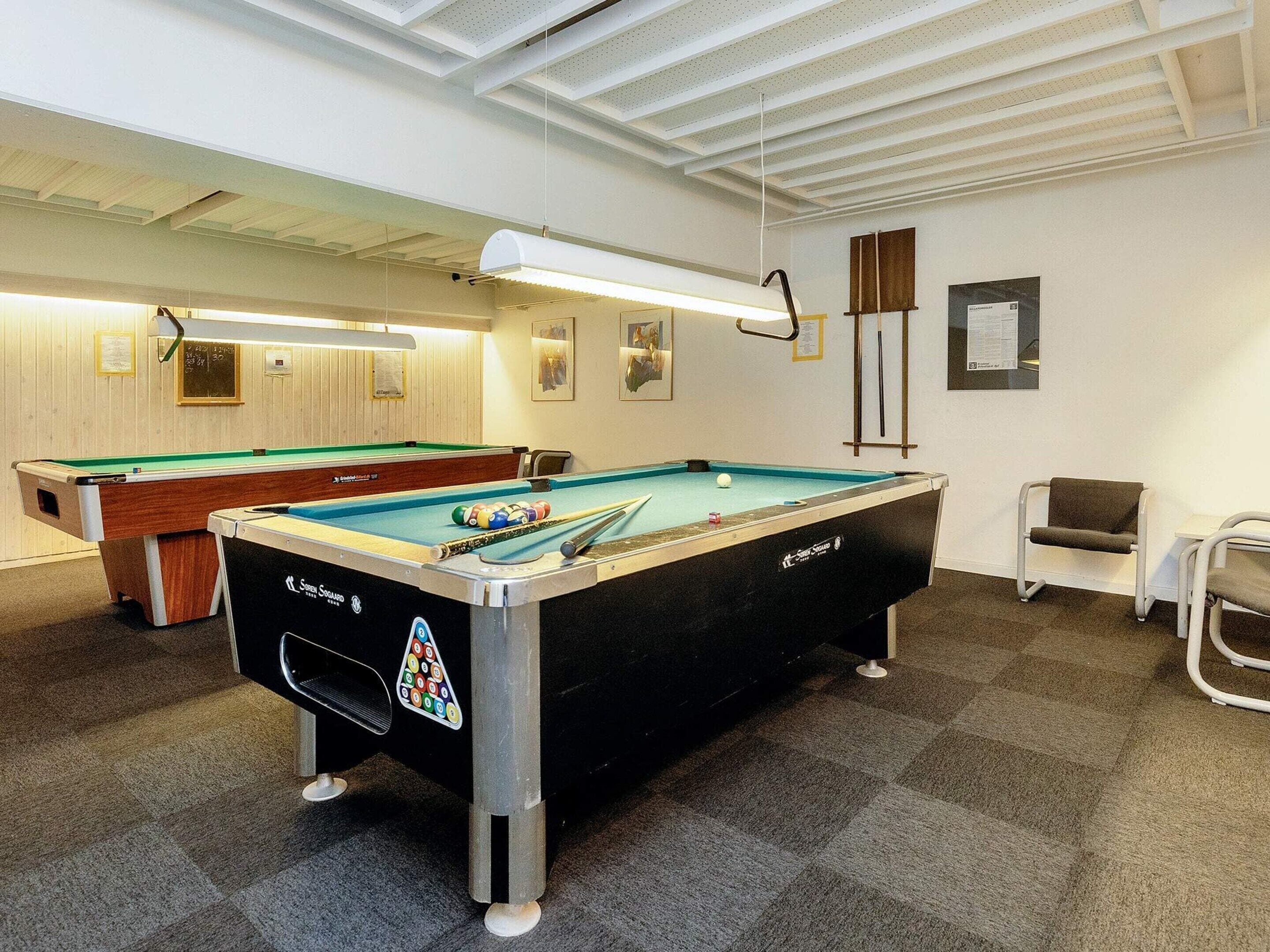 A pool table with a black and white design, a second pool table in the background, and a chair to the right.