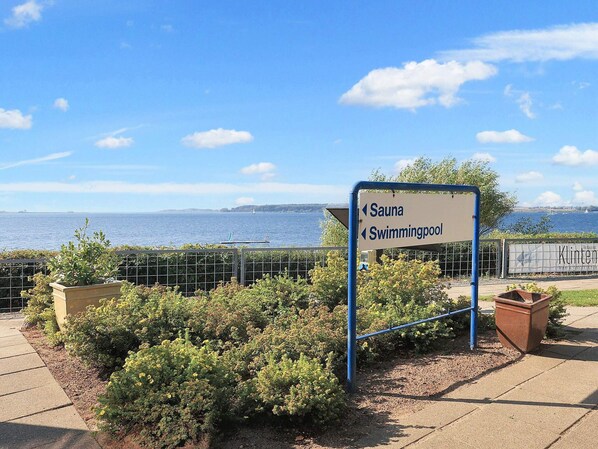 A sign indicating directions to a sauna and swimming pool, with a view of the sea and a restaurant named 'Klinten' in the background.