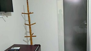 Une petite pièce, peu meublée, avec une porte coulissante, un porte-manteau en bois, une petite table avec une télécommande et un téléviseur fixé au mur.