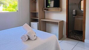 Une chambre à coucher avec un lit, un téléviseur fixé sur une étagère en bois, une armoire et une salle de bain visible à travers une porte ouverte.
