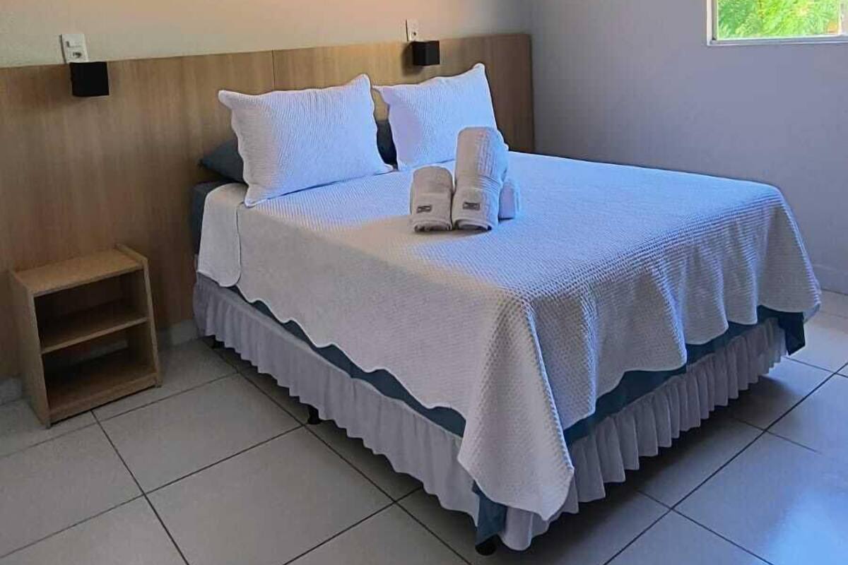 A neatly made bed with white linens, a wooden headboard, and a bedside table.
