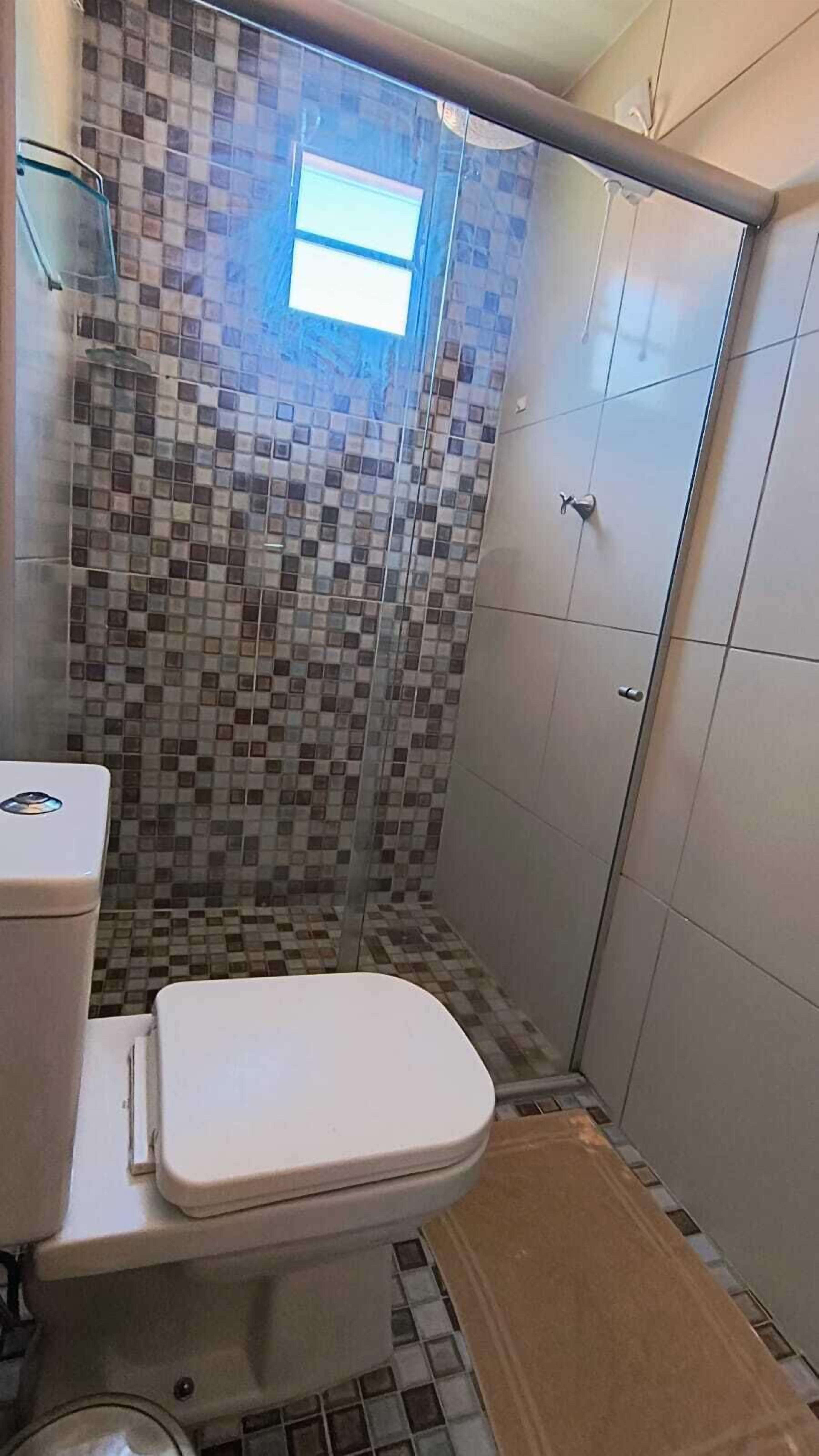 A bathroom with a toilet, a shower with a tiled wall, and a small window.