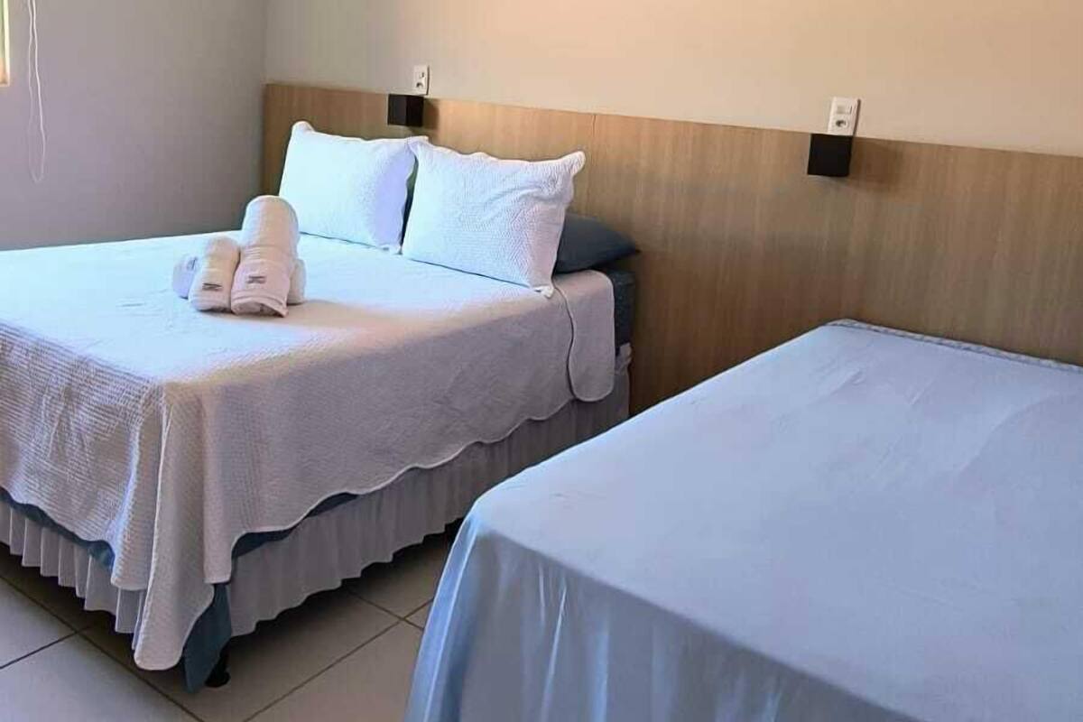 A hotel room with two beds, each with a white bedspread and pillows, a wooden headboard, and a wall-mounted air conditioning unit.
