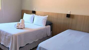 A hotel room with two beds, each with a white bedspread and pillows, a wooden headboard, and a wall-mounted air conditioning unit.