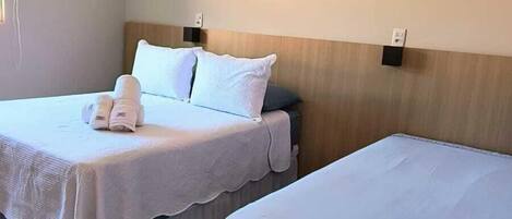 A hotel room with two beds, each with a white bedspread and pillows, a wooden headboard, and a wall-mounted air conditioning unit.