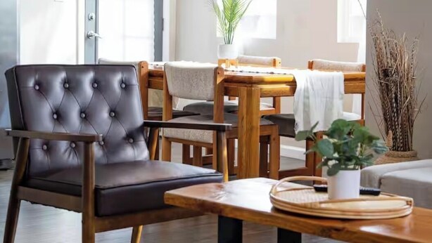 Un salon moderne avec un fauteuil en cuir, des meubles en bois, un luminaire en fibres tressées et une vue sur l’extérieur.