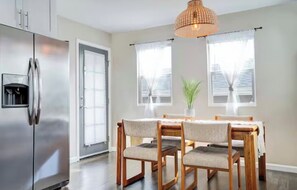 Eine moderne Küche mit einem Edelstahl-Kühlschrank, einem Holzespeisetisch mit vier Stühlen und einer hängenden Pendelleuchte.