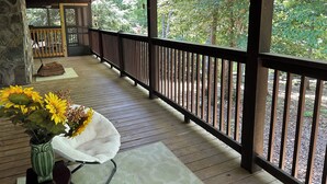 A wooden deck with a railing, a stone wall, and a view of trees.