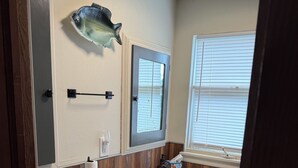Un baño con lavamanos blanco, tocador de madera, un adorno con forma de pez, un espejo y una ventana con persianas.