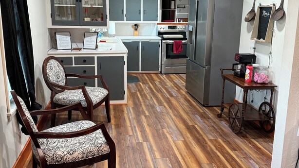 Una cocina con piso de madera, un comedor con sillas estampadas y un refrigerador.