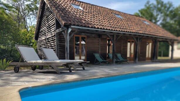 Eine Holzhütte mit Ziegeldach, Schwimmbecken und Liegestühlen.