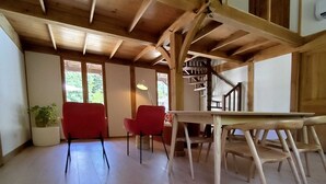 Ein geräumiges Zimmer mit hohen Decken, Holzbalken, einer Treppe und einem Essbereich mit Tisch und Stühlen.