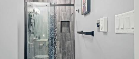 A modern bathroom with a glass shower enclosure, a wooden accent wall, and a white sink.