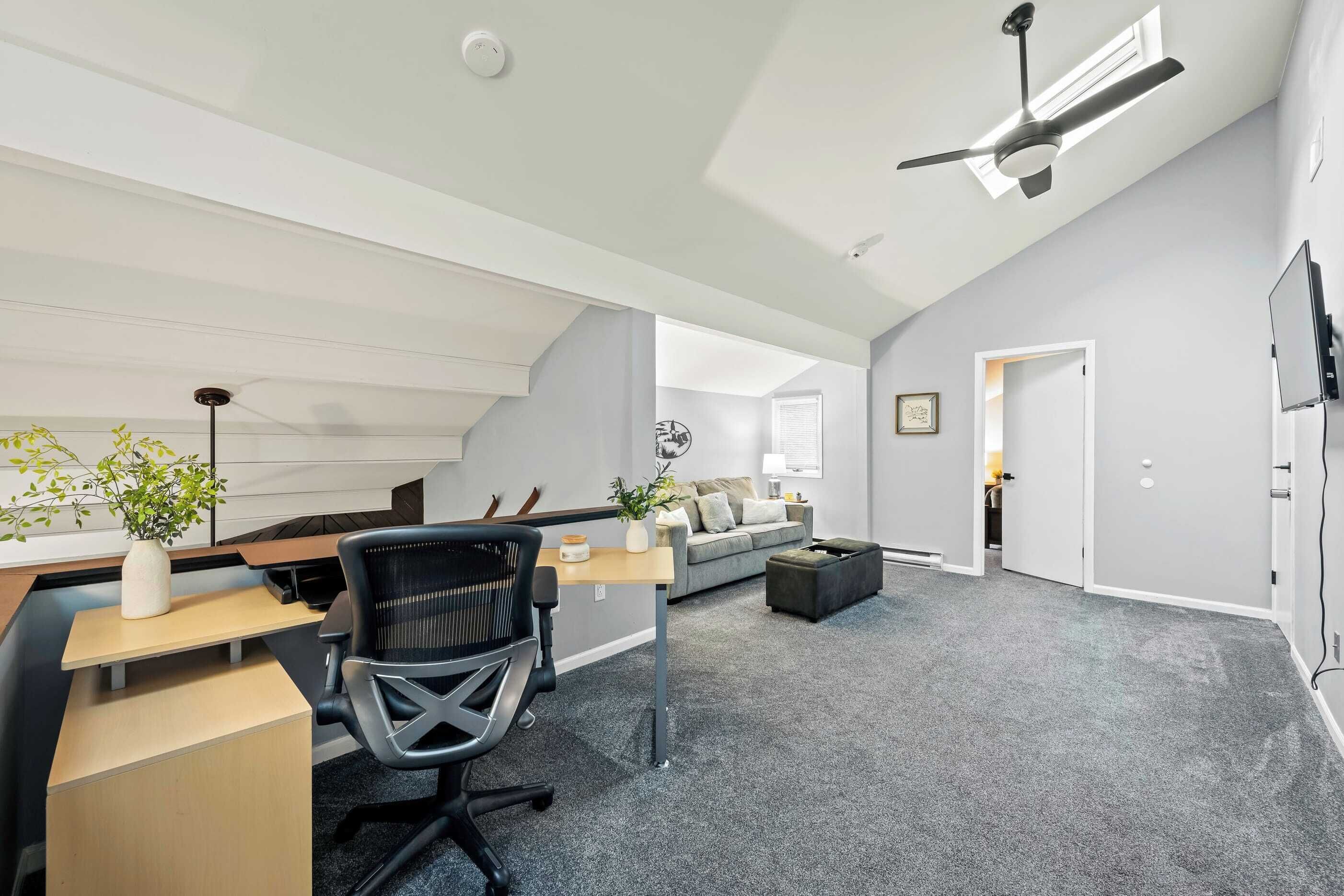 A modern loft-style room with a desk, office chair, and a living area with a sofa and a coffee table.