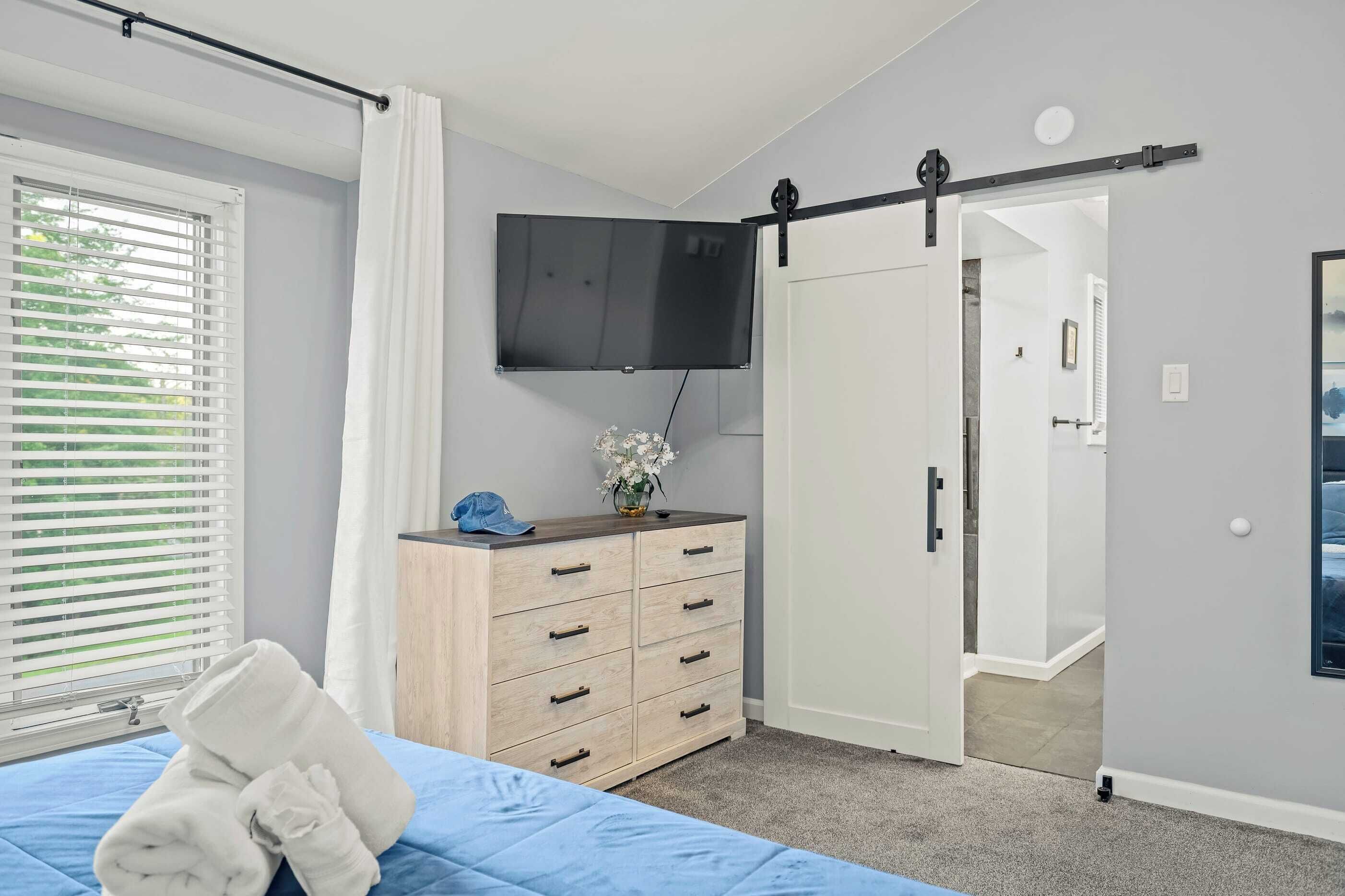 A bedroom with a bed, a dresser, a TV, and a sliding door.