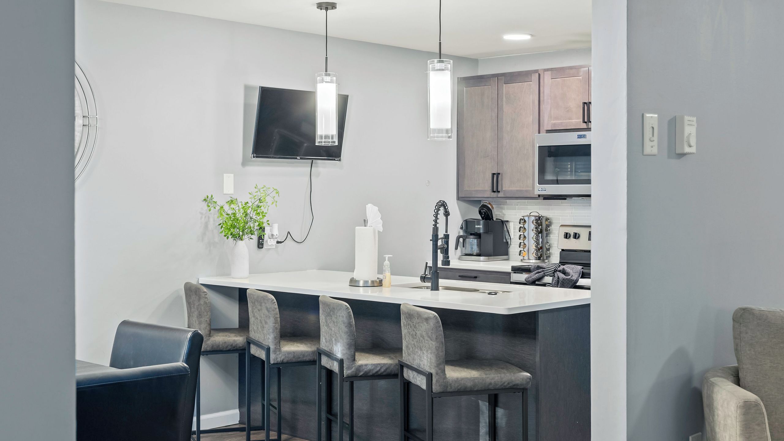 Una cocina moderna con una isla central, taburetes de bar, un televisor de pantalla plana y electrodomésticos integrados.