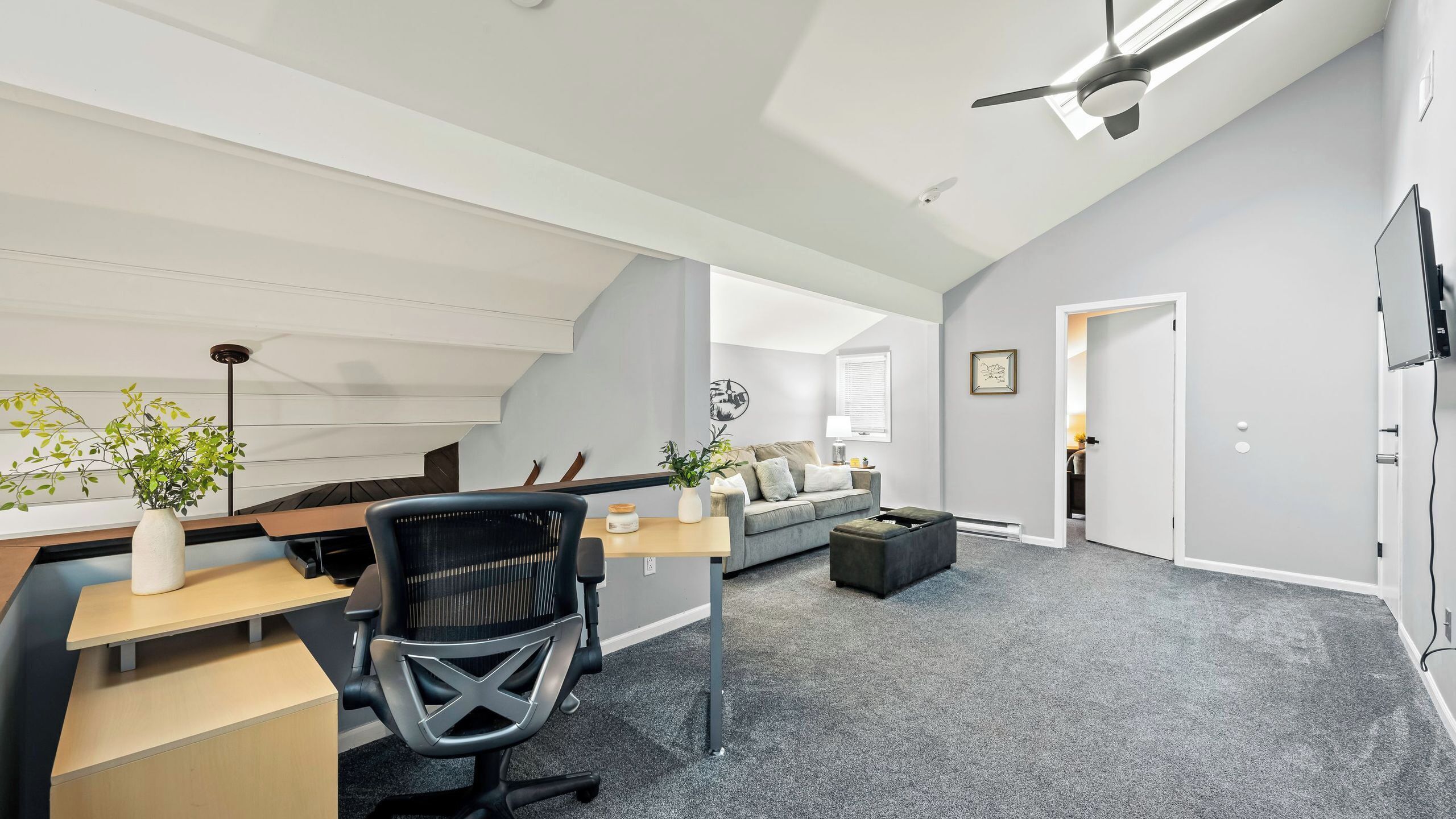 A modern loft-style room with a desk, office chair, sofa, and a staircase leading to an upper level.