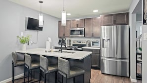 Una cocina moderna con una isla central, electrodomésticos de acero inoxidable y un televisor de pantalla plana en la pared.