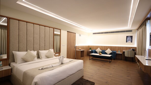A modern hotel room with a large bed, a sofa, a desk, and a mirror. - Rukman Hotels Jaipur (Jaipur)