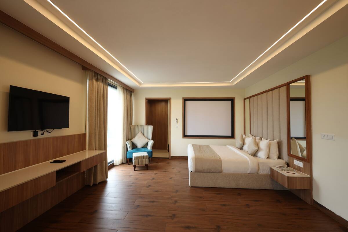 A modern hotel room with a flat-screen TV, a sofa bed, a bedside table, and a large mirror.