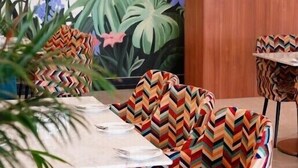 A dining area with a mural of tropical plants and colorful chairs with zigzag patterns. - Rukman Hotels Jaipur (Jaipur)