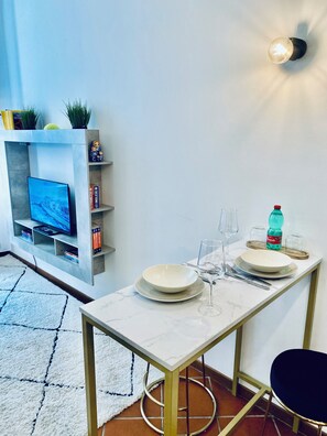Un coin repas avec une table dressée pour deux personnes, un téléviseur posé sur une étagère et un luminaire fixé au mur.