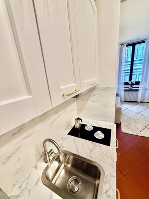 A modern kitchen with white cabinets, a stainless steel sink, and a marble countertop.