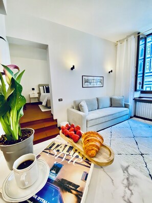 Una sala de estar moderna con un sofá, una mesa de centro con pasteles, una planta en maceta y una revista.