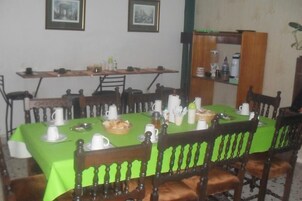 Un comedor con mantel verde, sillas de madera y distintos utensilios de comedor.
