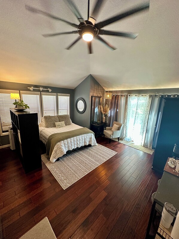 Une chambre à coucher avec un lit, un ventilateur de plafond, un bureau et une fenêtre avec des rideaux.
