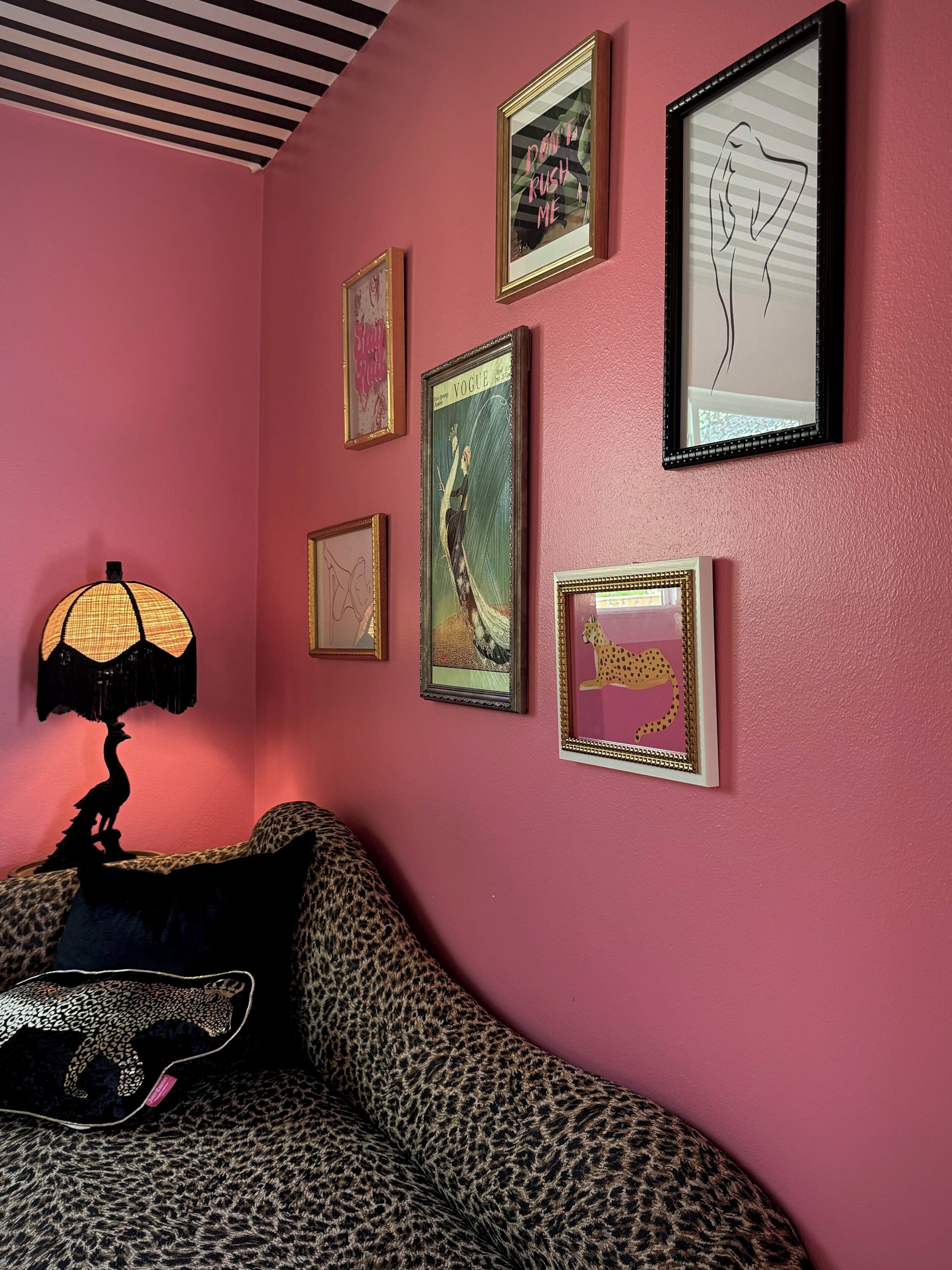 A room with a pink wall, a leopard print sofa, and several framed pictures.