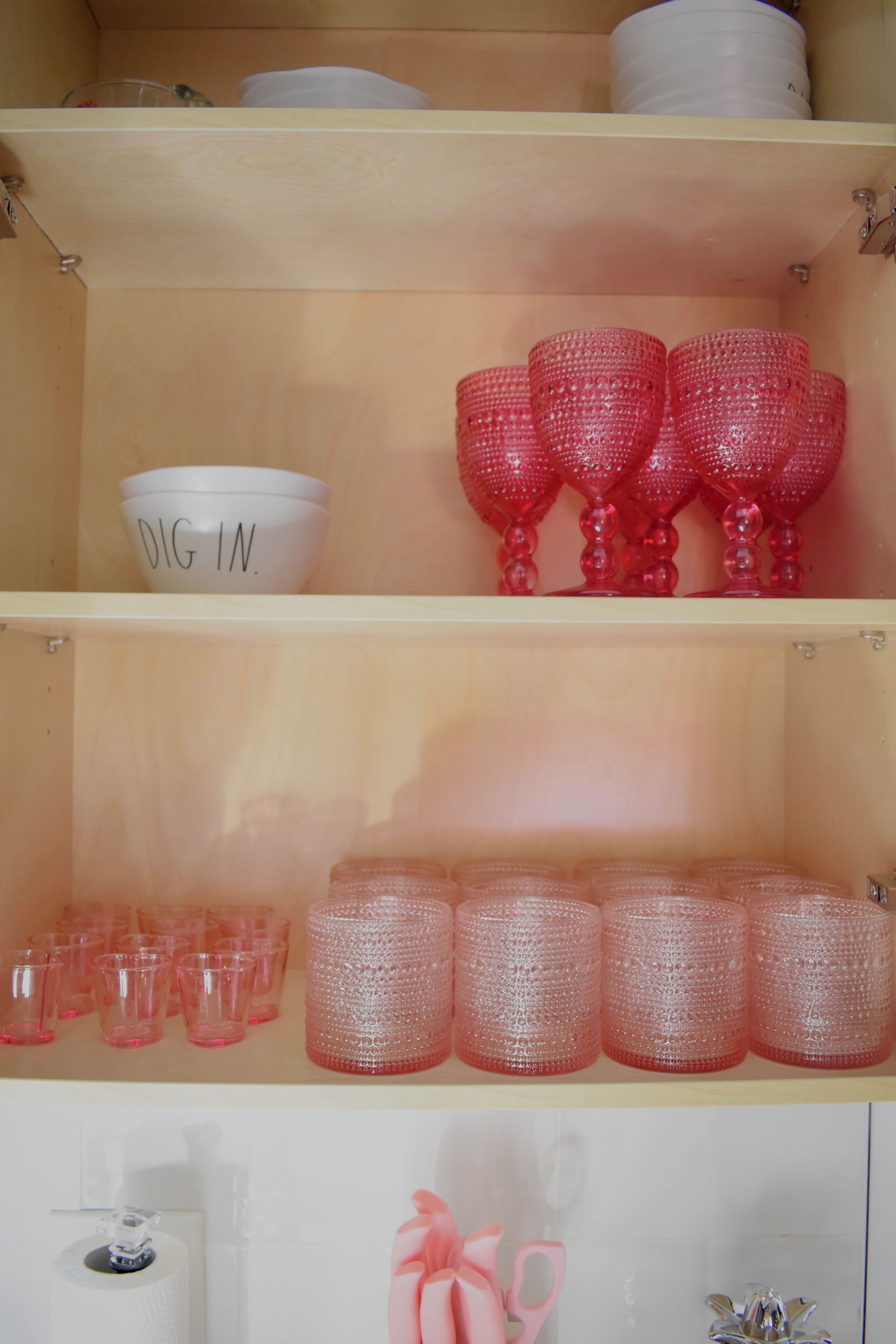 A shelf with various glassware, including a white bowl with "DIG IN" written on it, and several pink glasses.