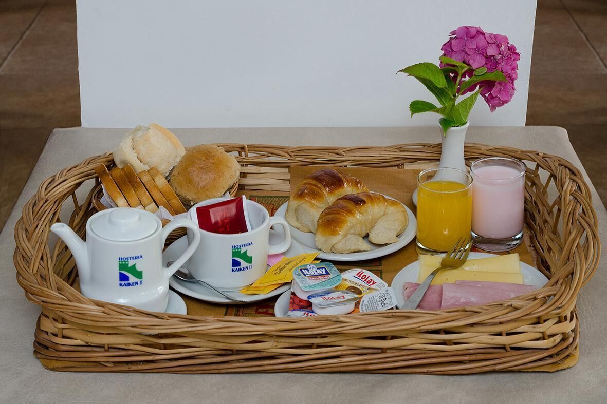A breakfast tray with bread, croissants, a teapot, a mug, juice, yogurt, cheese, and ham.