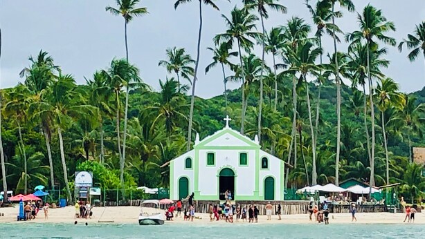 A beach with a small white church, palm trees, and people on the sand. - Beach House in Praia dos Carneiros/PE, one of the most beautiful beaches in Brazil (Tamandaré)
