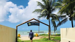 A pathway leading to a sign for 'Condomínio Prive Praia dos Carneiros' with a view of the ocean and palm trees. - Beach House in Praia dos Carneiros/PE, one of the most beautiful beaches in Brazil (Tamandaré)