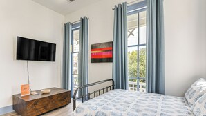 A bedroom with a bed, a wooden side table with a TV, and a window with curtains. - Walk to Strand District: Historic Galveston Home (Galveston)