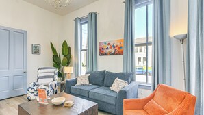 A living room with a blue sofa, an orange chair, a wooden coffee table, and a painting on the wall. - 1 Mi to Pleasure Pier: Golden-Age Getaway! (Galveston)