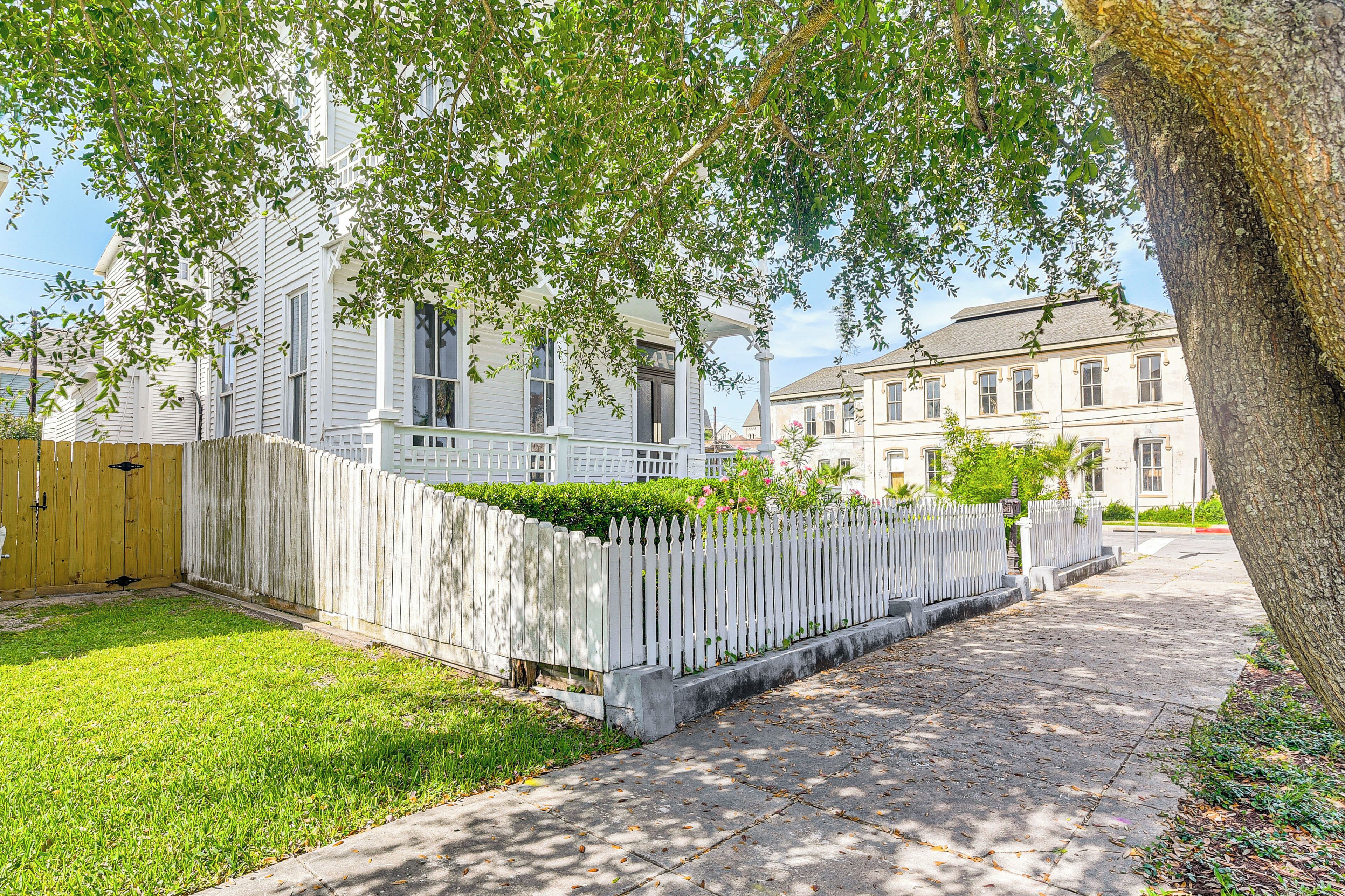 Une rue résidentielle bordée d’une clôture en bois peinte en blanc, avec une pelouse bien entretenue et des maisons dotées de grandes fenêtres.