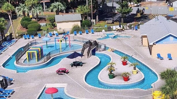 Una gran piscina al aire libre con varias pistas, tumbonas y un tobogán de agua.