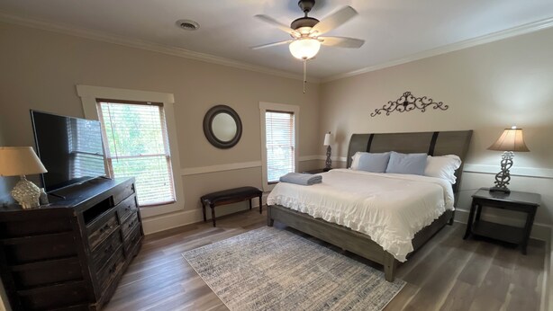 Une chambre à coucher avec un lit, une commode, un téléviseur, un ventilateur de plafond et une fenêtre.