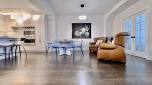 A modern kitchen with white cabinetry, a dining area with blue chairs, and a brown leather sofa. - Premium Loft 3BR&2BA • Heart of Downtown Boston • Guest Favorite (Boston)