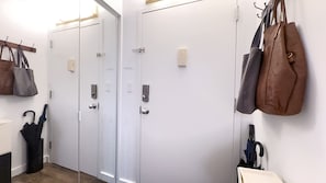 A hallway with three white doors, each with a keycard reader and a lock. There are handbags hanging on hooks on the wall, and an umbrella leaning against the wall.