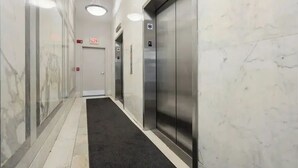 A hallway with marble walls, two elevators, and a black carpet. - Premium Loft 3BR&2BA • Heart of Downtown Boston • Guest Favorite (Boston)