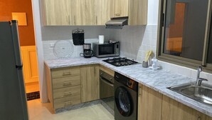 A compact kitchen with wooden cabinets, a built-in dishwasher, a microwave, a gas stove, and a sink. - Charming apartment for rent in Kenitra - Oriental & rustic style 🏡 (Kénitra)