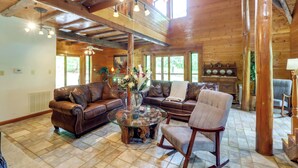 A spacious living room with a wooden ceiling, leather sofas, a glass coffee table, and a fireplace.